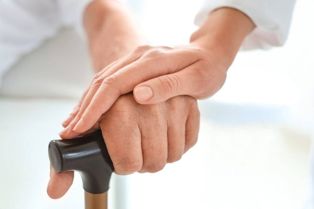 Caretaker's Hand Reassuring Elderly Patient's Hand on Cane